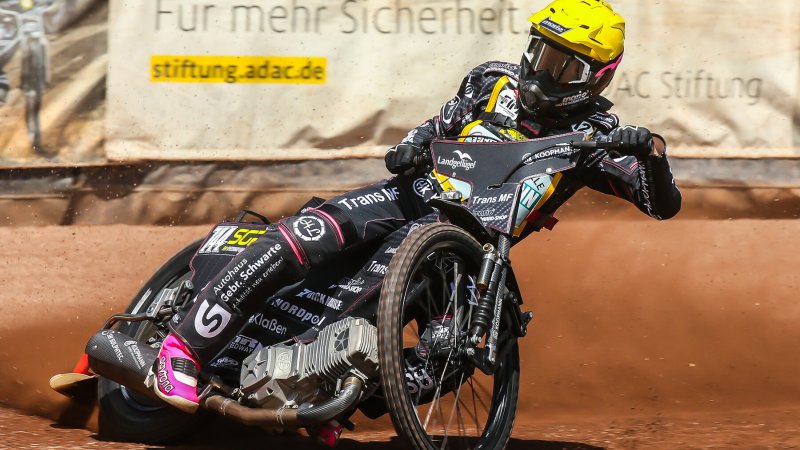 Fahrer mit gelbem Helm driftet vor der ADAC-Bande durch die Kurve