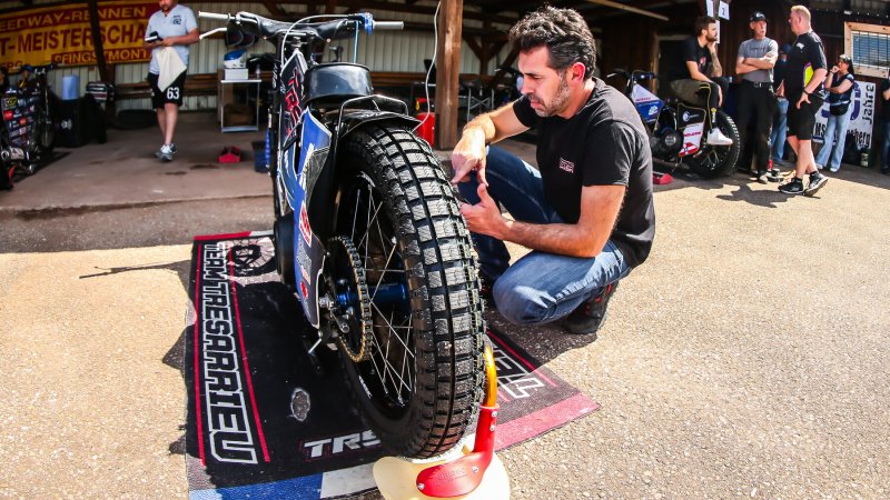 Mechaniker kniet am Hinterrad eines Speedway-Motorrads in der Box