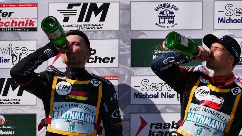 Zwei Fahrer feiern auf dem Podium mit Sekt