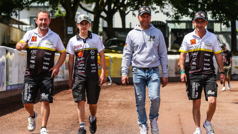 Vier Teammitglieder in Rennshirts gehen durch das Fahrerlager