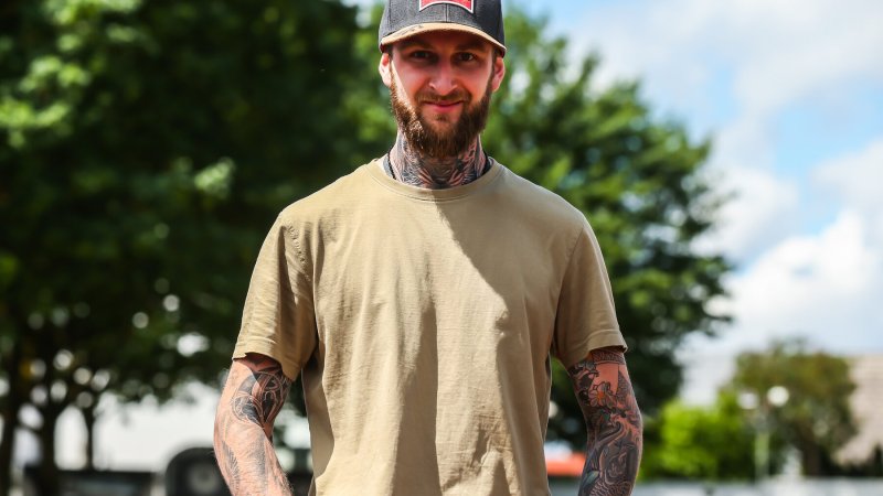 Speedway-Fahrer mit Kappe und tätowierten Armen im Fahrerlager