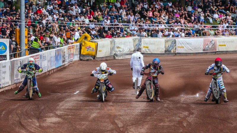 Vier Fahrer am Startband vor der vollen Tribüne