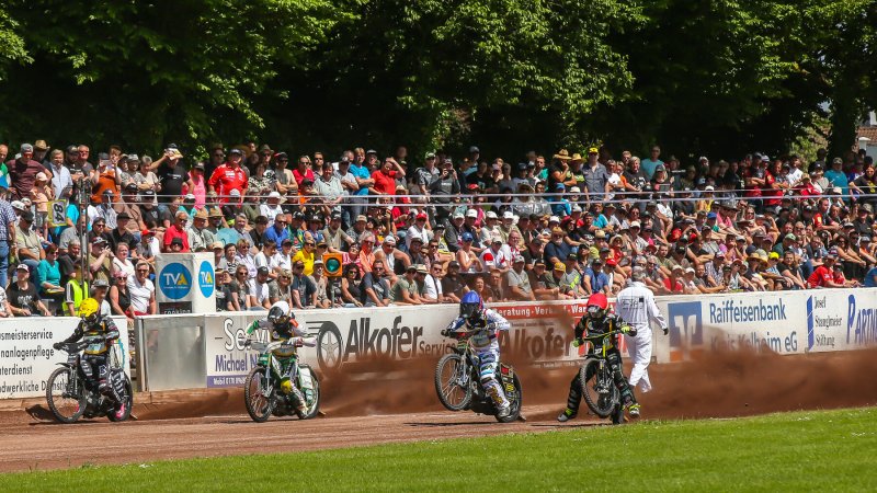 Vier Fahrer im Rennen vor der vollbesetzten Tribüne